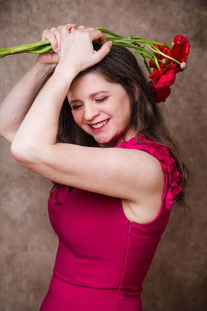 Woman holding red flowers above her head during playful 40th birthday studio photoshoot in London portrait studio
