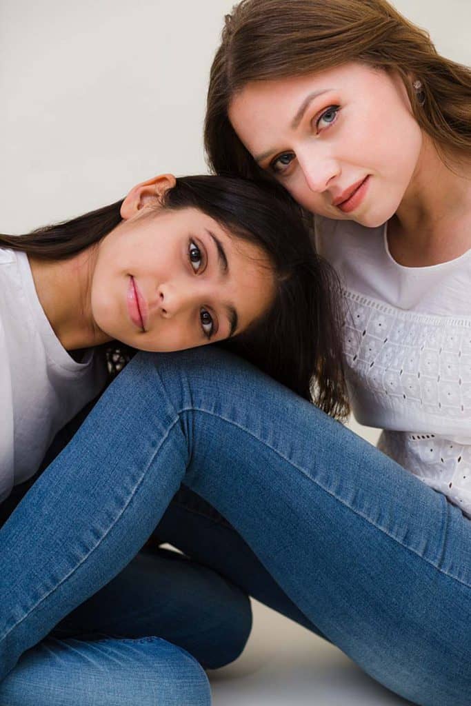 Relaxed mother and teenage daughter portrait in white shirts and blue jeans, showing a natural and intimate bond.