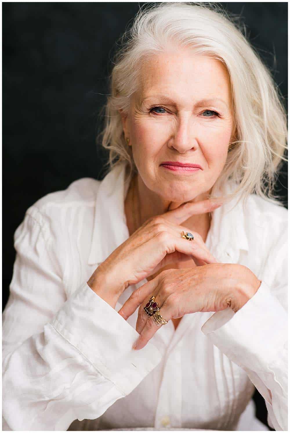 professional-portrait-of-middle-age-woman-with-silver-hair-in-white-shirt-chin-leaning-on-hands-by-high-end-photographer-london