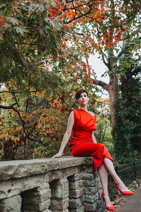 Environmental portrait of a woman in red dress seated outdoors in a London park